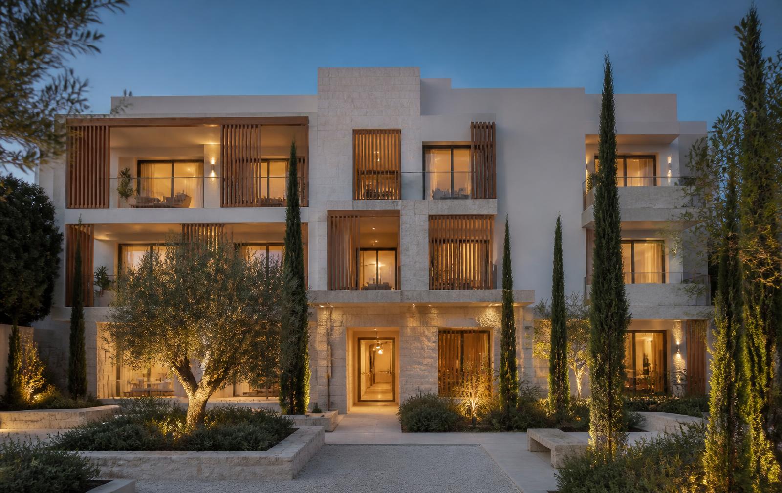 Three-storey white and limestone building at dusk, oak balcony screens and a lit courtyard with olive and cypress trees